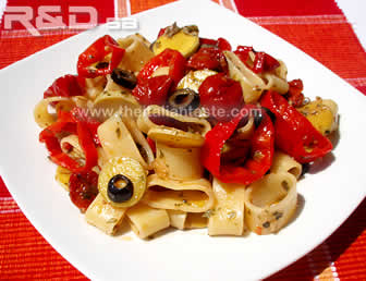 pasta fredda con verdure, la foto mostra la pasta calamarata con anelli di peperoni dolci e zucchine a trombetta in fette e olive nere e ciliegini sott'olio