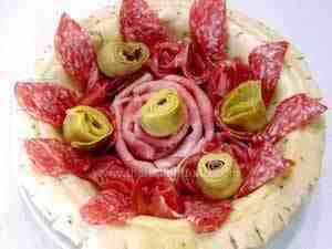 The image shows a bowl made with bread dough filled with Italian salami: raw and boiled ham, salami and artichokes