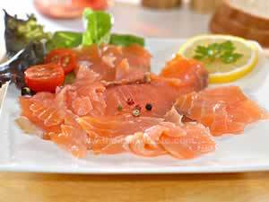 salmon carpaccio, paper-thin salmon slices are arranged on a white serving plate