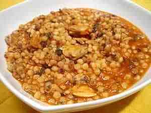 fregula with clams (fregola con arselle<9, the photo shows a little bowl filled with pasta fregola dressed with tomatoes and shelled clams