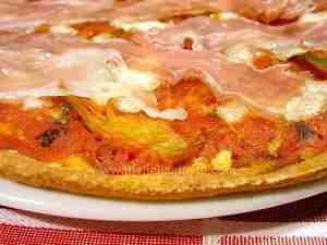 Detail of pizza whose topping is artichoke-and-tomato sauce with slices of prosciutto