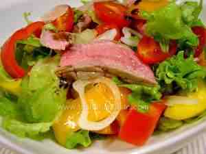 beef salad made with meat, bell peppers, tomatoes, onion and green leaves on a platter